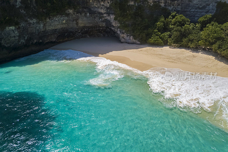 Nusa Penida岛，Kelingking海滩。俯视图鸟瞰图的沙质干净的海滩，清澈的蓝色和蓝绿色的水。带着白色泡沫的岩石和海浪